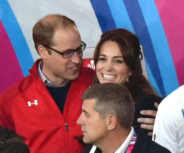 "Two people smiling at a rugby event, with colorful background stripes."