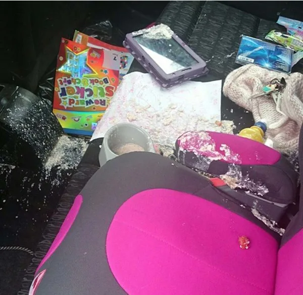 Messy car backseat with spilled cereal, a tablet, coloring book, and scattered items.