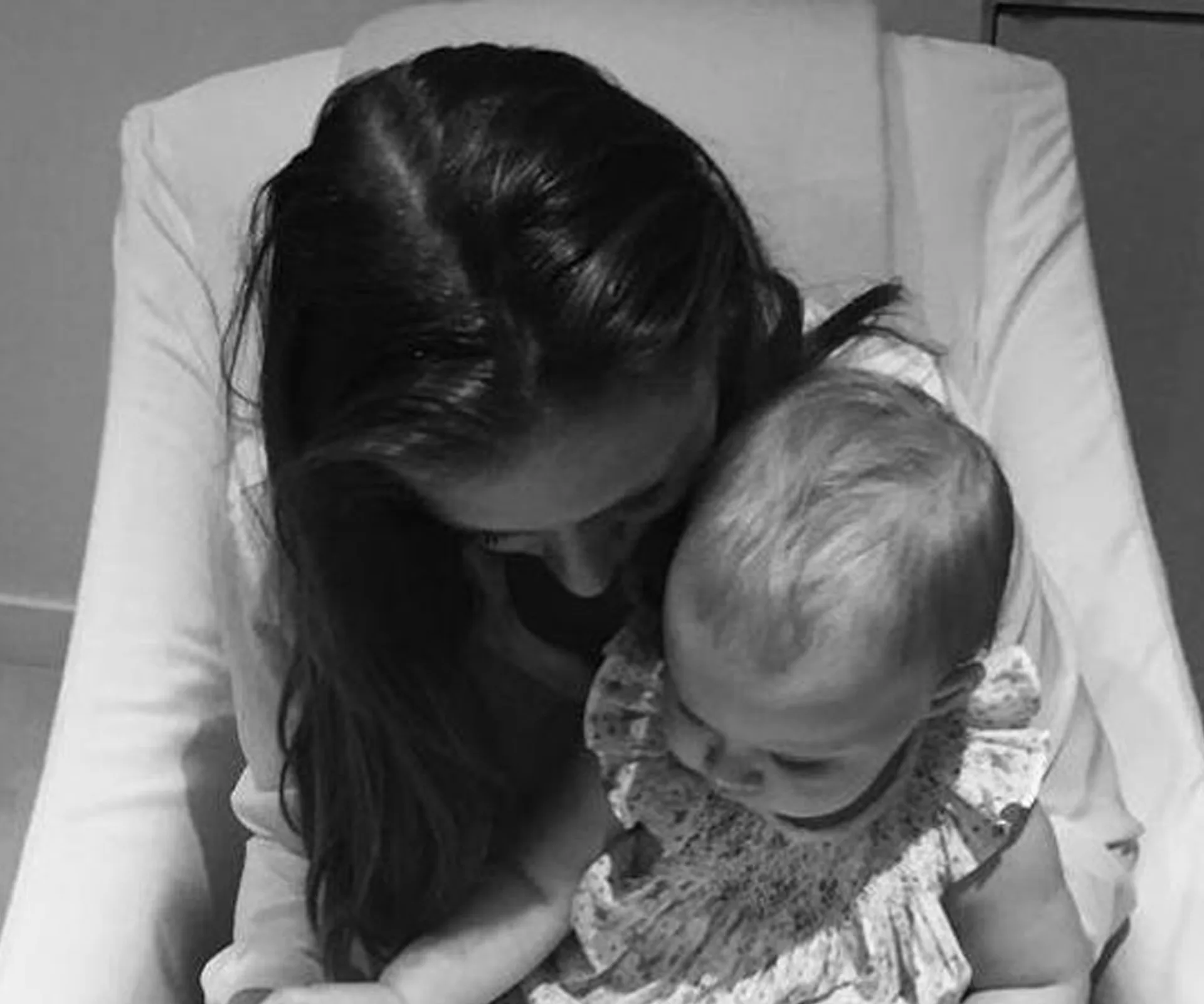 Mother holding her baby close, both are looking down, in a tender moment of affection.