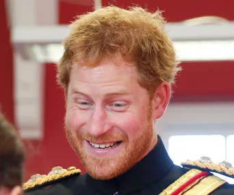 A man with red hair in a uniform smiling widely in a brightly lit room.