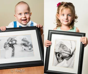 Two young children holding framed photos of themselves as premature babies in hospital settings.