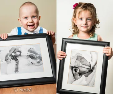 Two young children holding framed photos of themselves as premature babies in hospital settings.