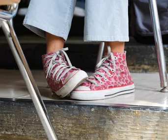 Close-up of pink high-top sneakers with heart pattern under a desk.