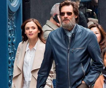 People walking on a city street; man with sunglasses and a beard, woman with long hair in a light jacket.