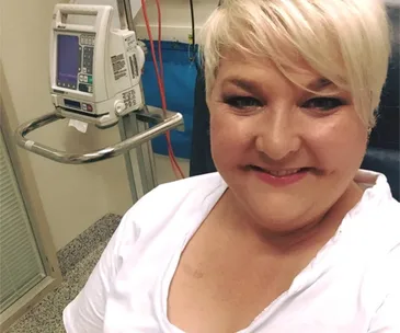 Woman smiling in a hospital setting with medical equipment in the background.
