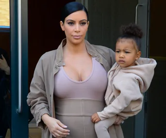 Woman in beige outfit holding a young child, both looking outside.