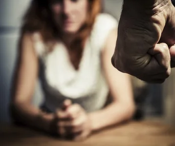 Blurry woman sitting at table with clenched fist in foreground, implying tension or conflict.
