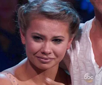 Bindi Irwin on "Dancing with the Stars," emotional expression, wearing a light-colored outfit, stage lights in the background.