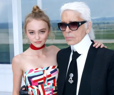 Lily-Rose Depp at Fashion Week in a colorful dress, standing with Karl Lagerfeld in sunglasses and a black suit.