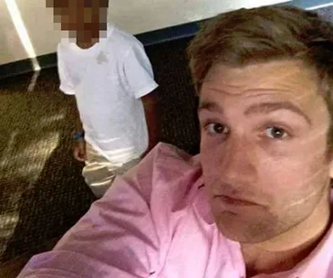 A man in a pink shirt takes a selfie with a young child in a white shirt whose face is blurred.