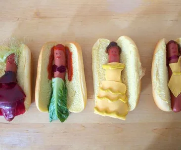 Hot dogs dressed as Disney princesses with vegetable accessories representing different gowns and hairstyles in buns.