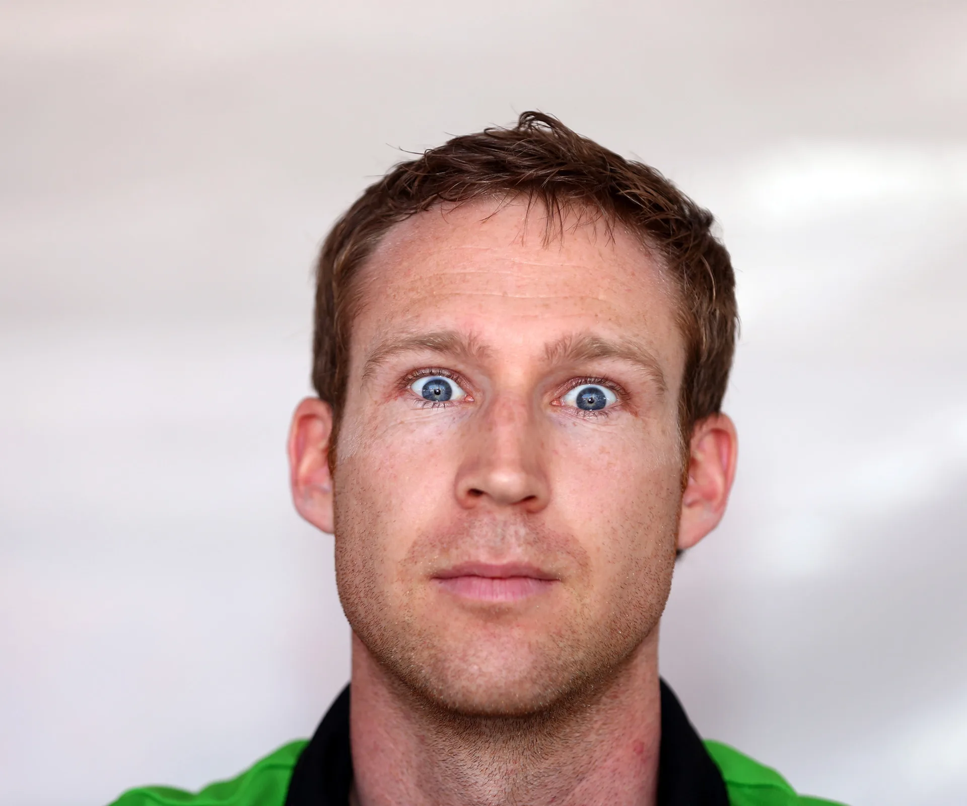 Face of a man with short hair, wearing a green shirt, looking directly at the camera with a neutral expression.