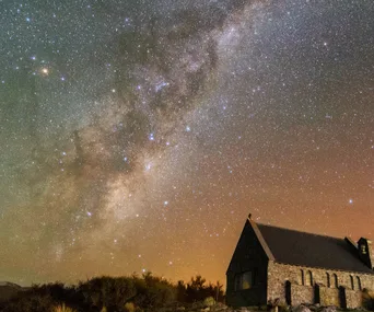Aurora australis lights up night sky over a stone church surrounded by stars.