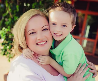Mother and young son smiling together outdoors, embracing warmly.