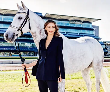 Woman in black suit holding a white horse's reins at a racecourse.