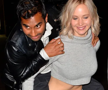 Two people smiling and posing together, with one person wearing a gray sweater and the other in a leather jacket.