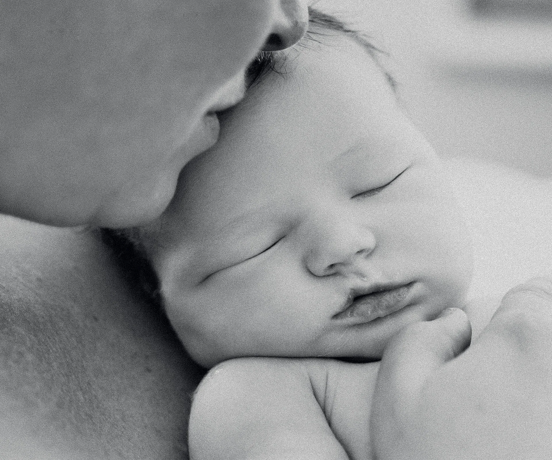 "Black and white photo of a sleeping baby being gently cuddled close by an adult, conveying tenderness and peace."