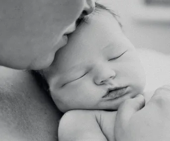 "Black and white photo of a sleeping baby being gently cuddled close by an adult, conveying tenderness and peace."