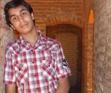 A young person in a plaid shirt stands in a narrow brick corridor, looking towards the camera.