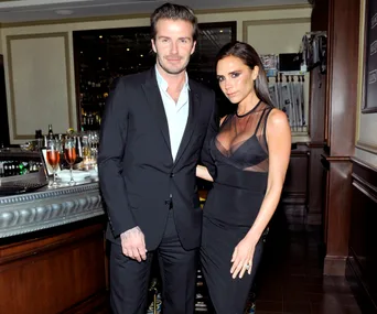 A couple in formal attire stands together in a sophisticated bar setting with drinks on the counter.