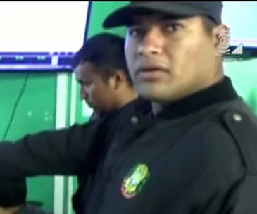 Security guard in uniform looks surprised in a control room with another guard in the background.