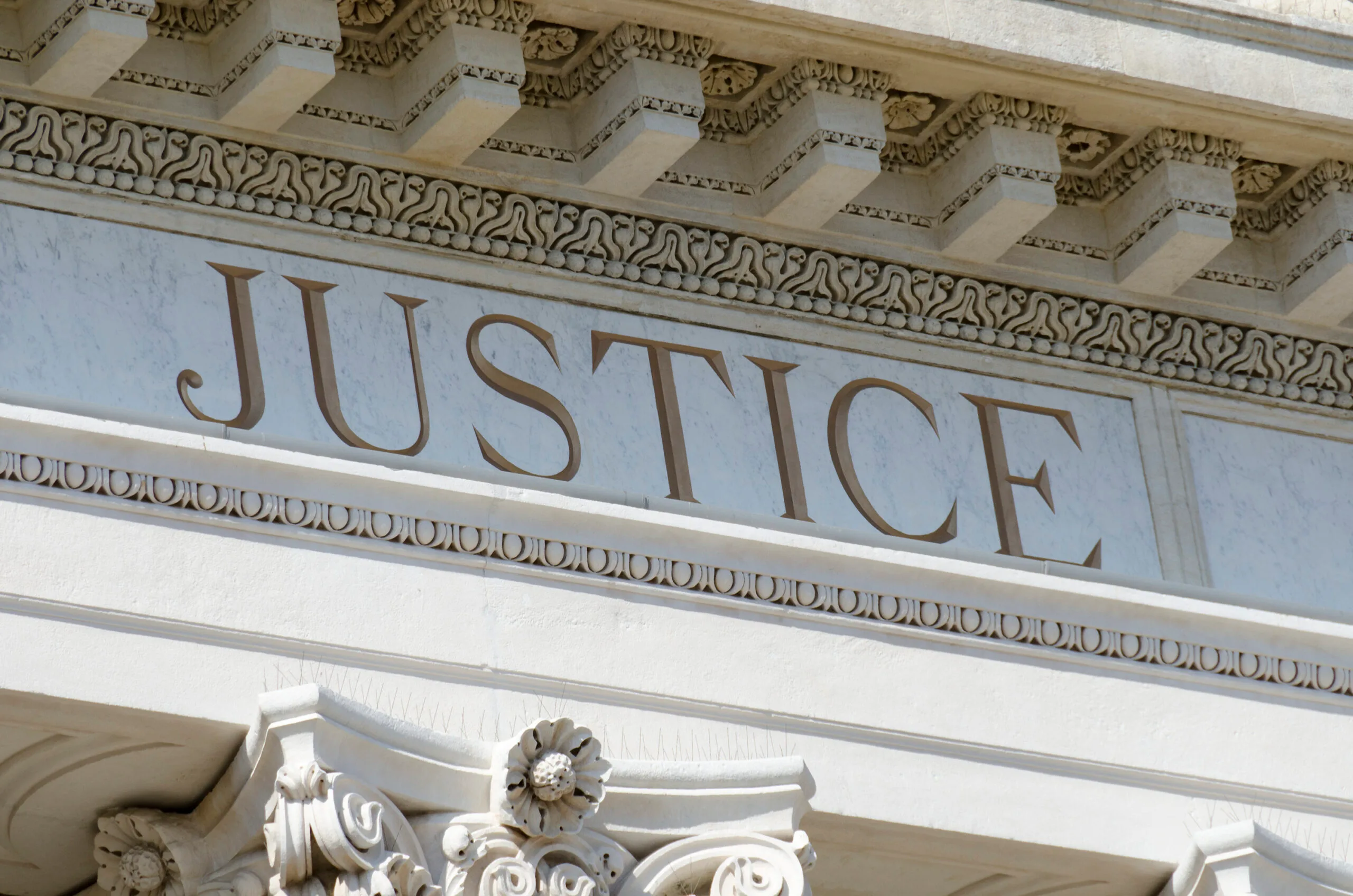 "Stone building facade with the word 'Justice' engraved, ornate details below a decorative cornice."