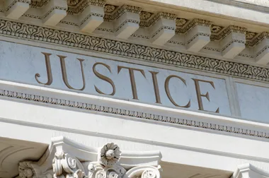 "Stone building facade with the word 'Justice' engraved, ornate details below a decorative cornice."