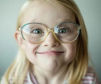 Smiling girl with round glasses and blonde hair, close-up.