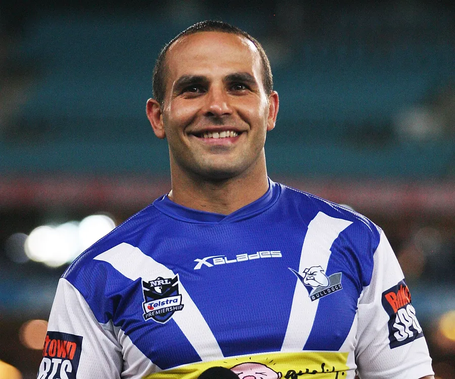 Smiling person in a blue and white sports jersey, with stadium lights blurred in background.
