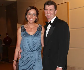 A couple posing together, the woman in a blue dress and the man in a black tuxedo, smiling at a formal event.