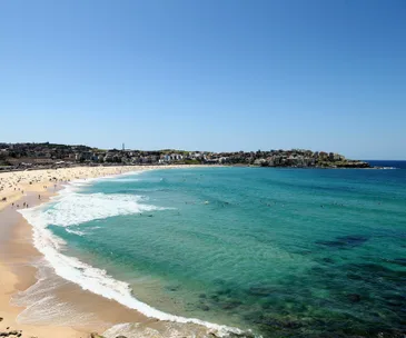 Aerial view of a crowded beach with people swimming in the clear turquoise water under a bright blue sky.