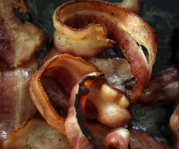 Close-up of sizzling, crispy bacon strips in a pan.