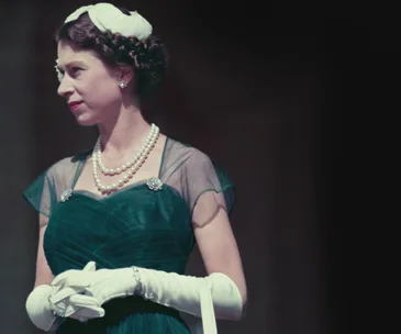 A woman in a teal gown with a pearl necklace and gloves, looking to the side, exuding elegance and poise.
