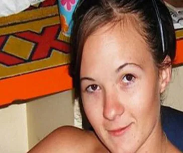 Young woman sitting indoors, with a slight smile, wearing a headband, and colorful items visible in the background.