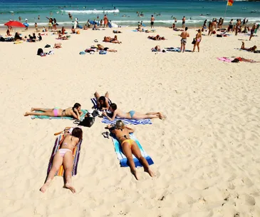 "People sunbathing on a crowded beach with blue sea and surfboards in the background."