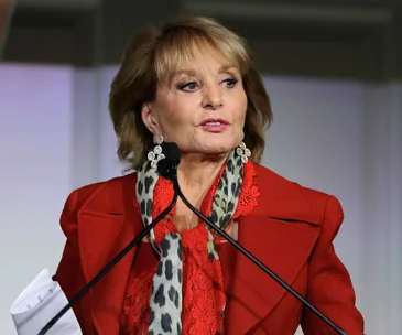 Barbara Walters speaking at an event, wearing a red outfit with a leopard print scarf.