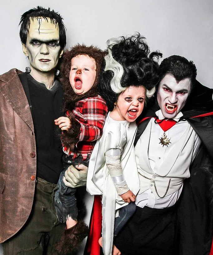 Family dressed as Frankenstein, Bride of Frankenstein, Dracula, and a werewolf, all in detailed Halloween costumes.