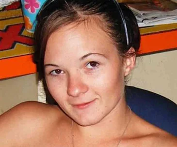 Young woman with brown hair, wearing a black headband, smiling slightly at the camera indoors.
