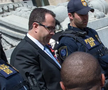 Man in suit detained by police officers outside a building.