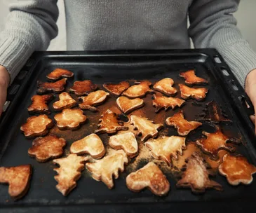 Person holding a tray of slightly burnt Christmas-shaped cookies, including trees and hearts.