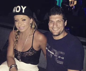 Young woman in a "BOY" cap and man smiling in a dimly lit setting.