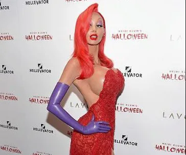 Jessica Rabbit costume with red dress, purple gloves, and orange hair at a Halloween event backdrop.