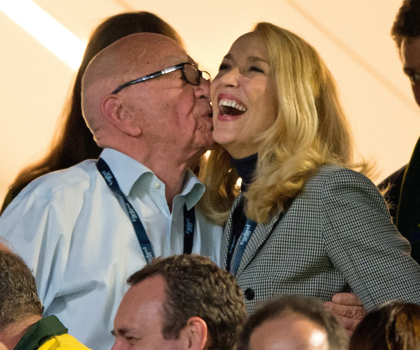 Couple at an event with one giving a kiss on the cheek, both smiling and wearing formal attire with lanyards.