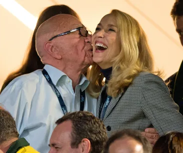 Couple at an event with one giving a kiss on the cheek, both smiling and wearing formal attire with lanyards.