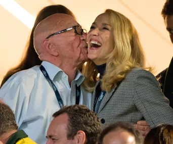 Couple at an event with one giving a kiss on the cheek, both smiling and wearing formal attire with lanyards.