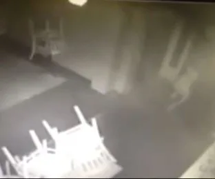 CCTV footage of a dimly lit nightclub with overturned chairs and a ghostly figure in the background.