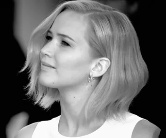 Jennifer Lawrence in profile, wearing elegant earrings, with short blonde hair and a thoughtful expression.