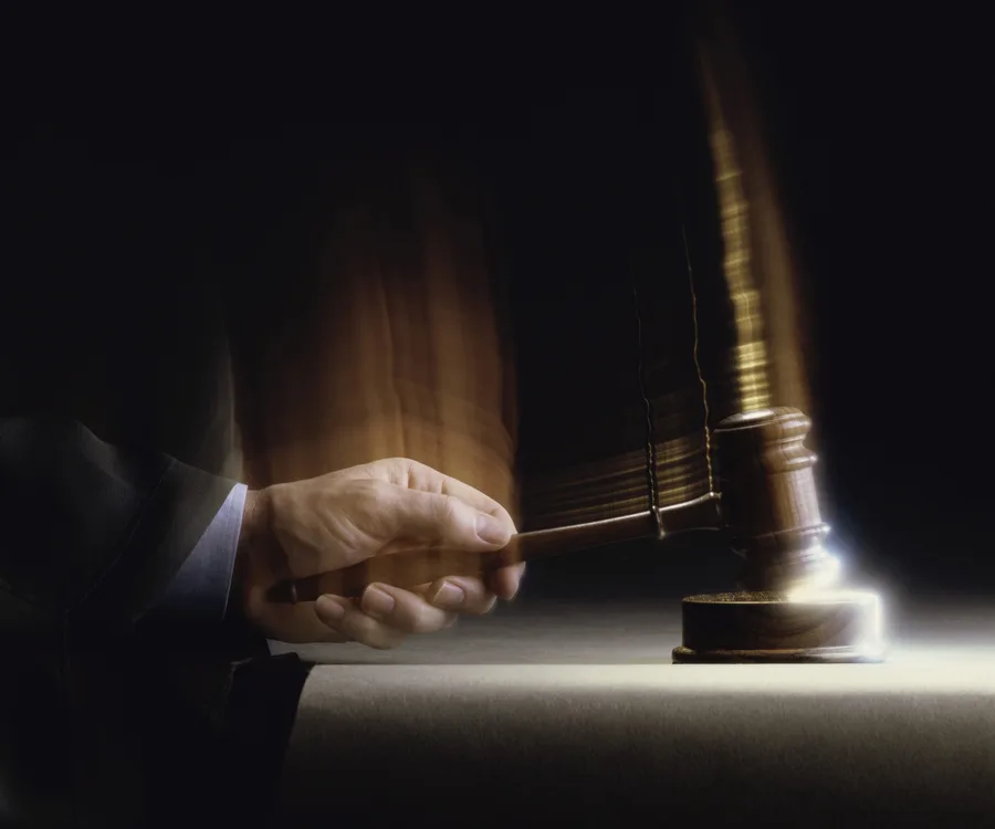 Judge’s hand holding gavel, striking in motion, creating a blurred effect on dark background.