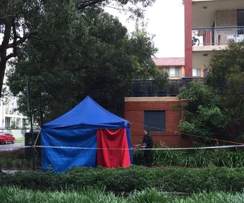 Police tent set up near a building, surrounded by trees and caution tape in Sydney.