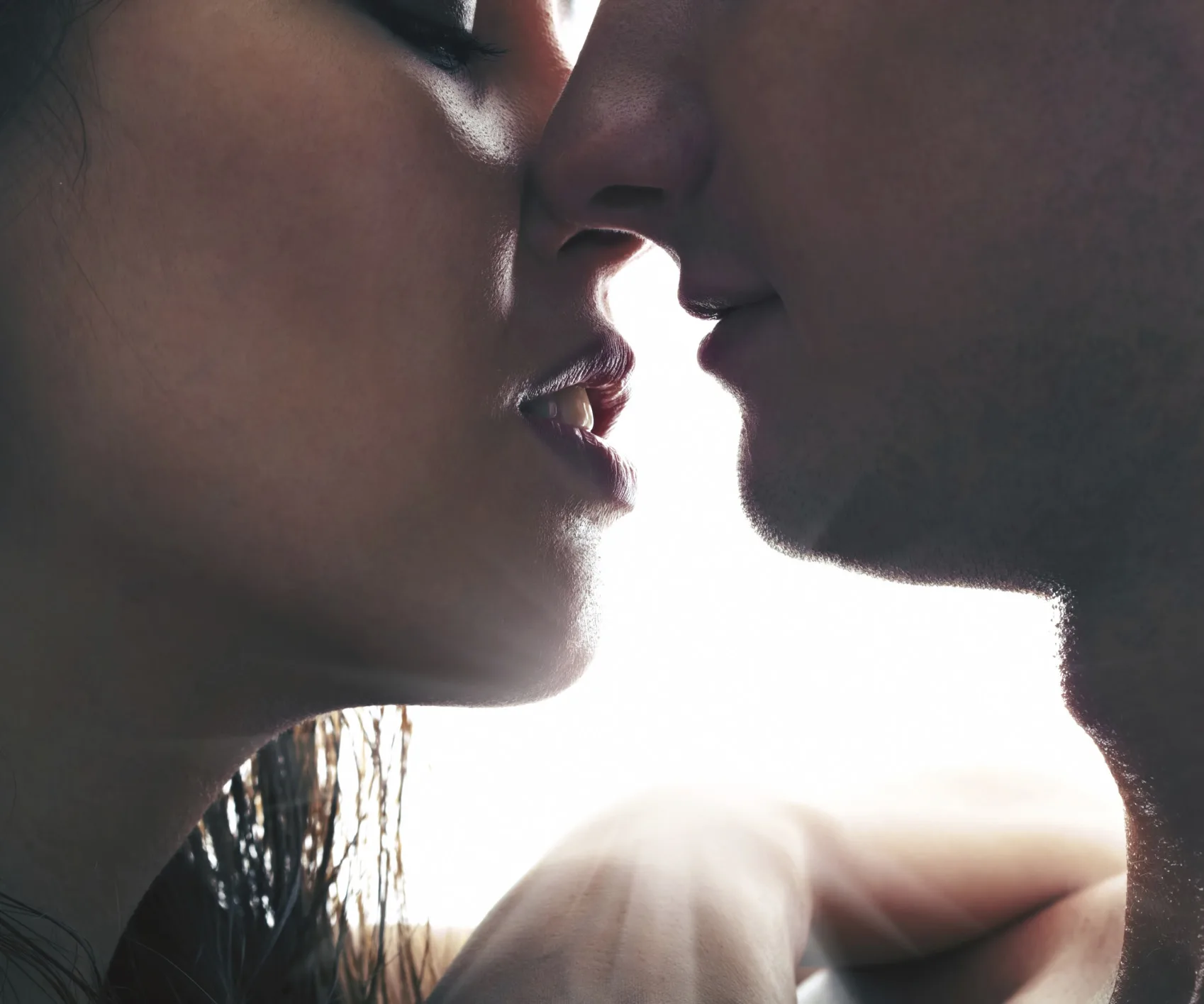 A man and woman face each other closely, about to kiss, against a bright white background.